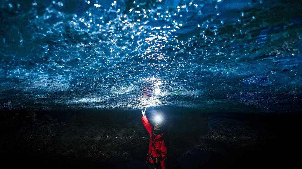 Une personne vêtue d’une veste rouge, sous l’eau, pointant une lampe de poche vers le haut. 3