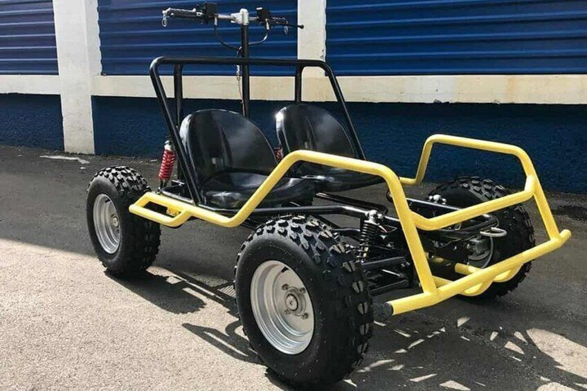 A yellow off-road vehicle with black seats and large tires parked in front of a blue building. 2
