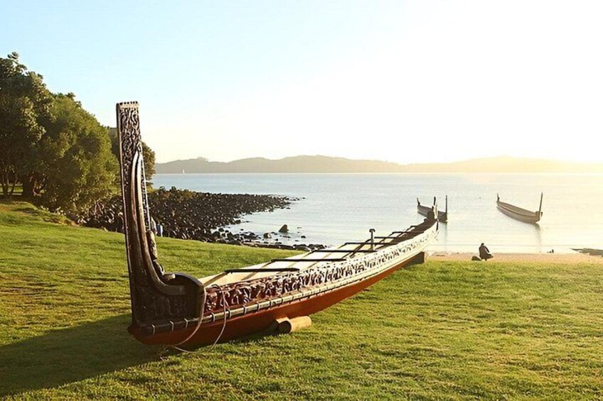 A model boat on a grassy field with a calm body of water and boats in the background. 2
