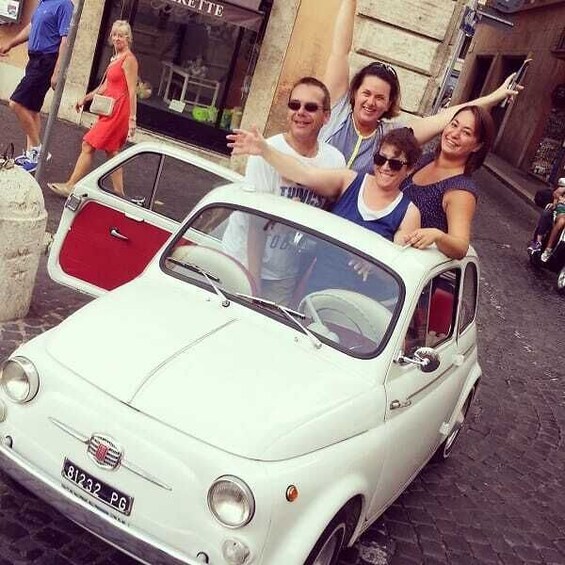 A vintage white car parked on a cobblestone street with people posing around it. 1