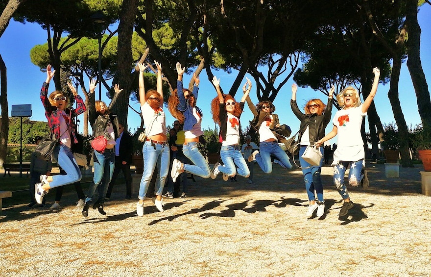 A group of people jumping in a park with trees and a clear sky. 5