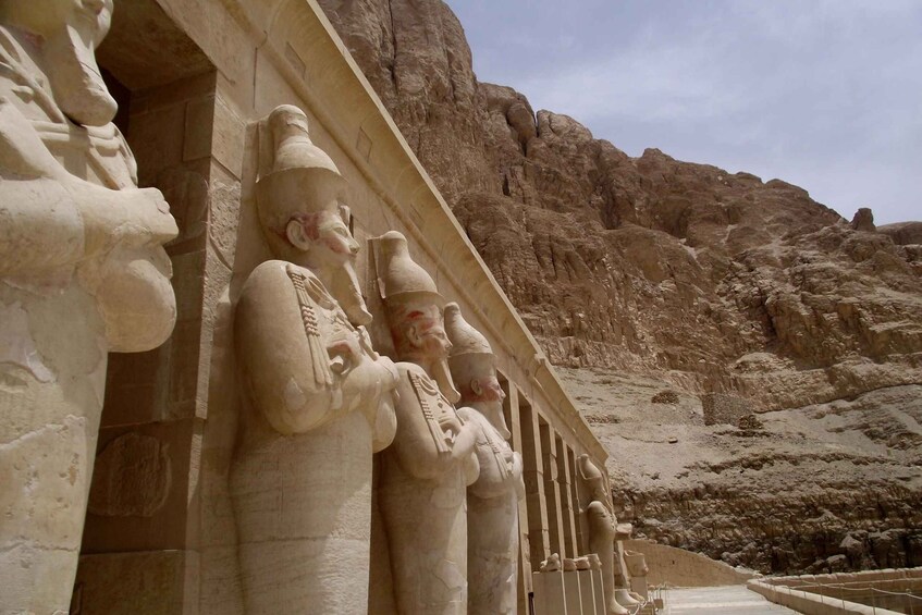 A series of large stone statues along a corridor with a rocky desert landscape in the background. 1
