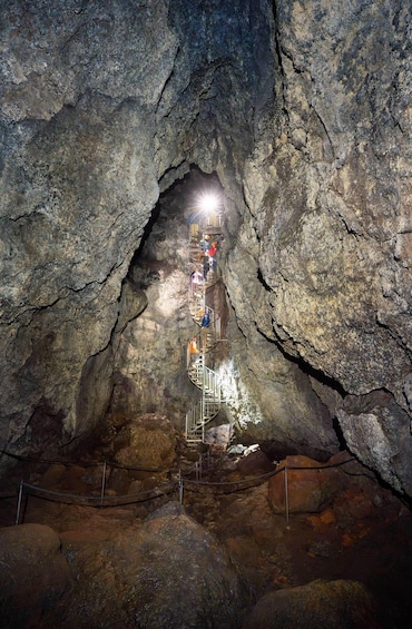 A cave with a metal staircase leading to a light source at the top. 1