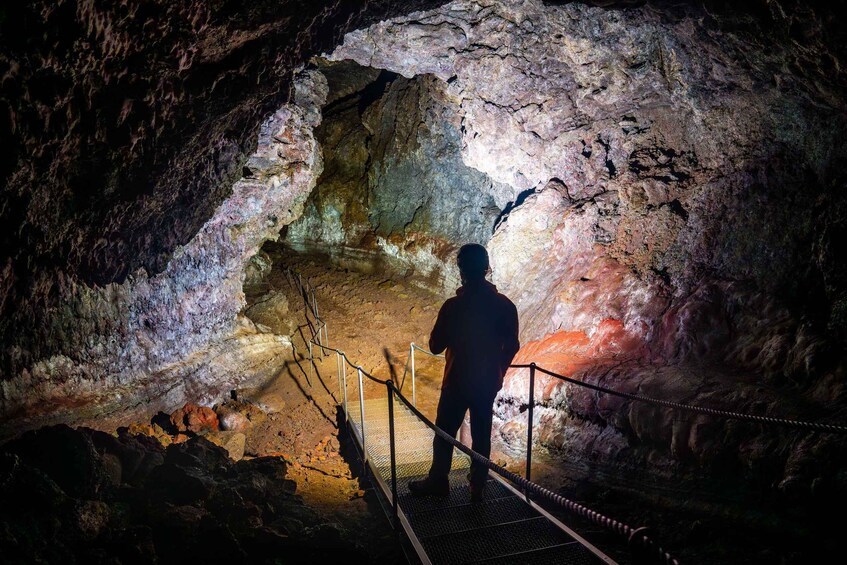 A person standing on a metal staircase inside a cave with rock formations and a light source. 2