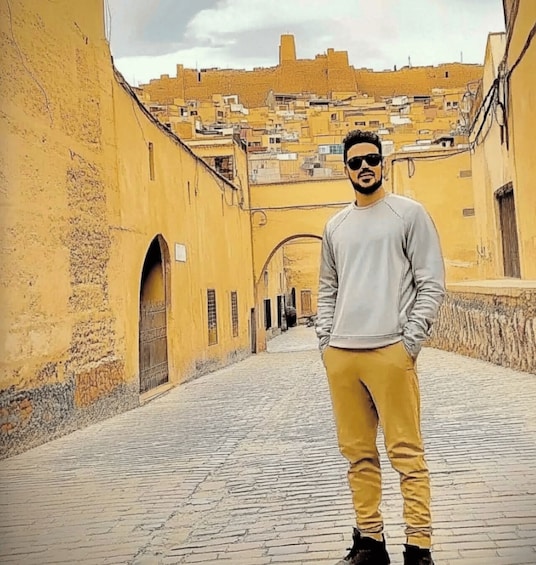A person standing in a narrow street with yellow buildings and a clear sky. 1