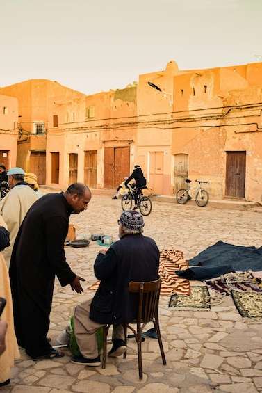 A cobblestone street with people, a bicycle, and a chair in an outdoor setting. 3