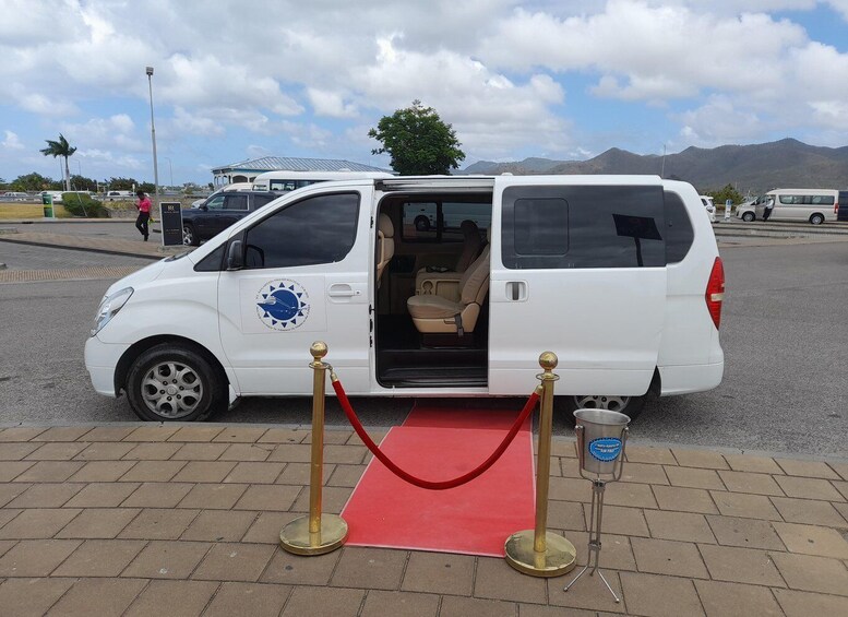 A white van with its door open, parked on a red carpet with gold stanchions, in a parking lot with mountains in the background. 3
