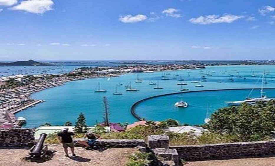 A coastal town with a marina filled with sailboats, a clear blue sky, and a distant mountain. 5