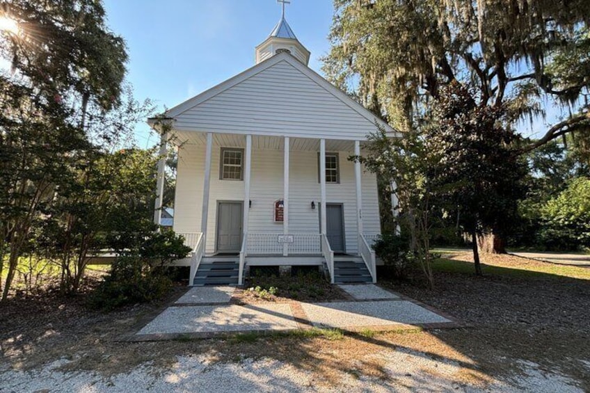 A white church with a steeple, surrounded by trees and a gravel path. 1