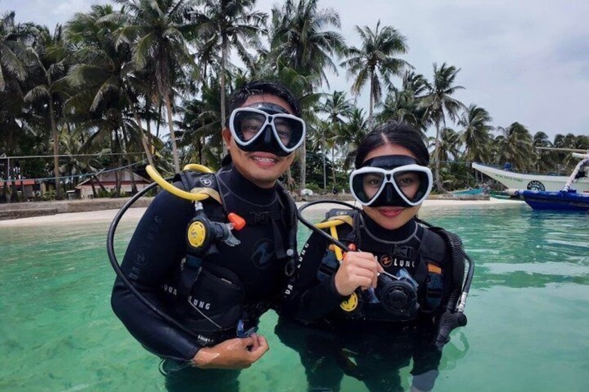 Dos personas con equipo de buceo, un océano azul cristalino y palmeras al fondo. 3
