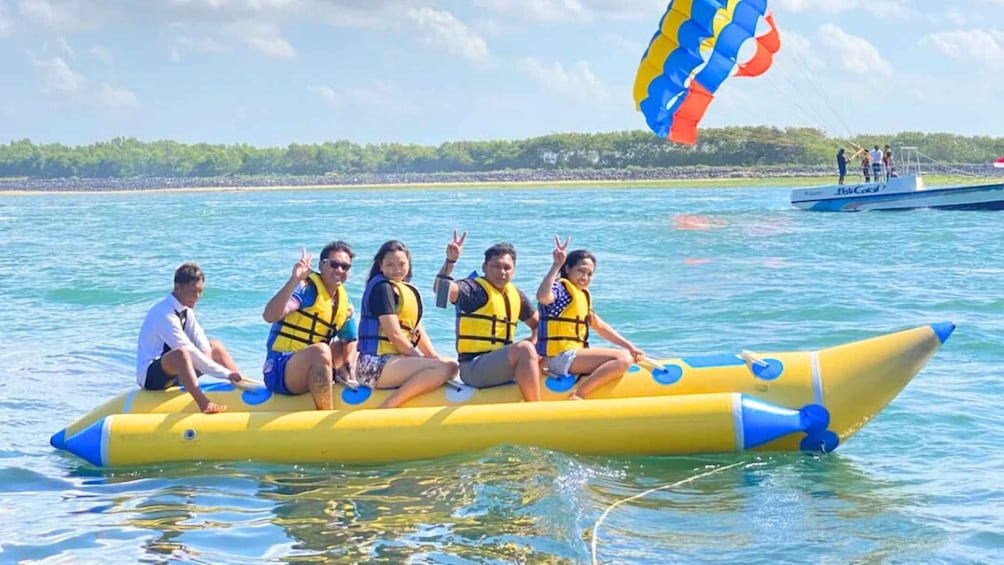 People on a yellow raft with blue accents, wearing life jackets, on a calm body of water with a clear sky. 2