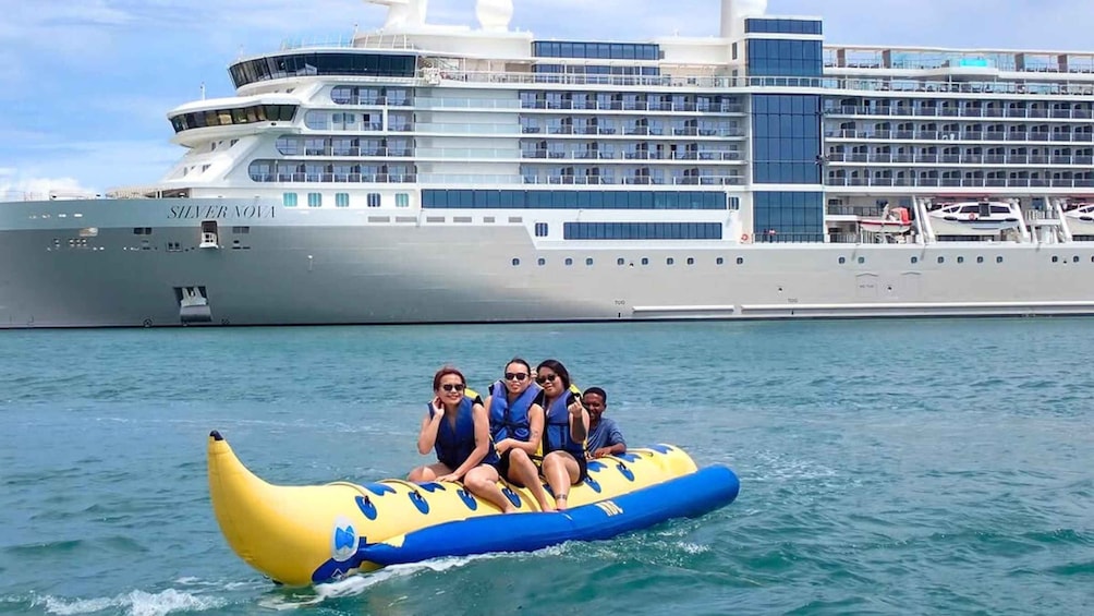 A group of people on a banana boat in the ocean with a cruise ship in the background. 1