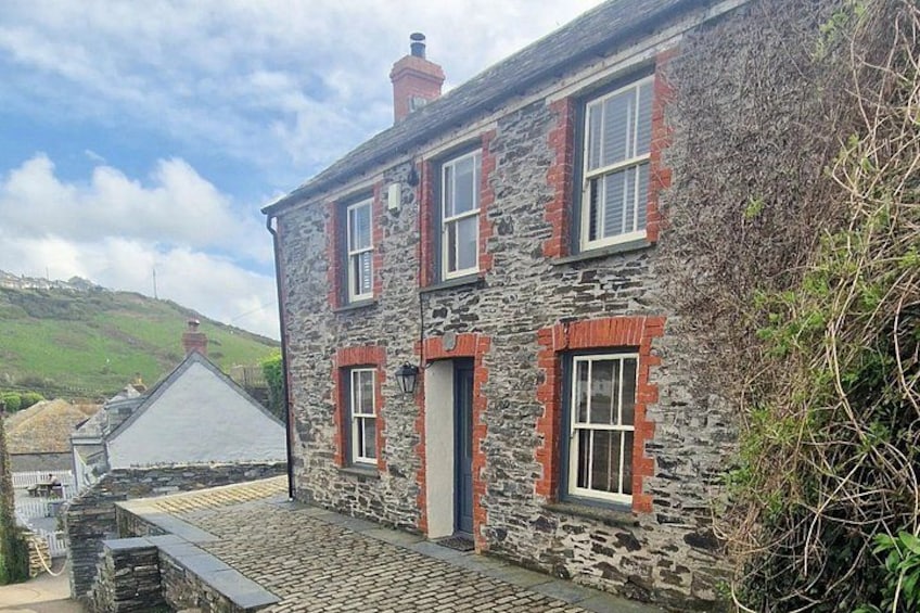 A stone house with red brick accents, a cobblestone path, and a hillside in the background. 5
