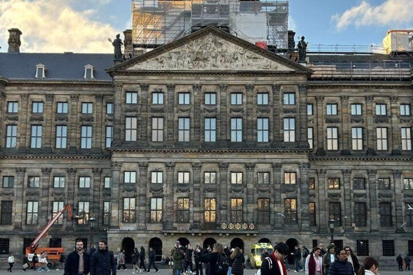 Een historisch gebouw met klassieke architectuur, een menigte mensen en steigers op de achtergrond. 2