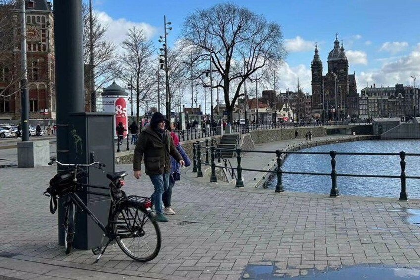 Een voetpad langs een rivier met een fiets, een tramhalte en historische gebouwen op de achtergrond. 5