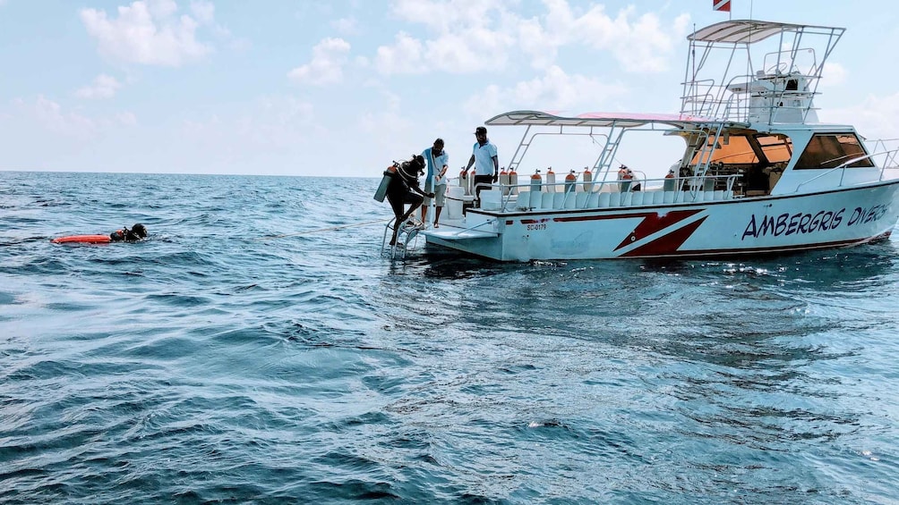A boat named 'AMBERGRIS DIVES' with people on board and a person in the water wearing a life jacket. 5