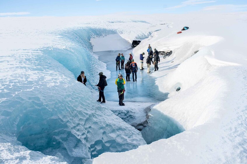 A group of people standing on a snow-covered glacier with a crevasse. 3