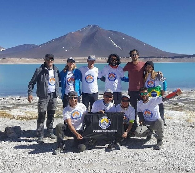 A group of people posing in front of a mountain and lake. 1