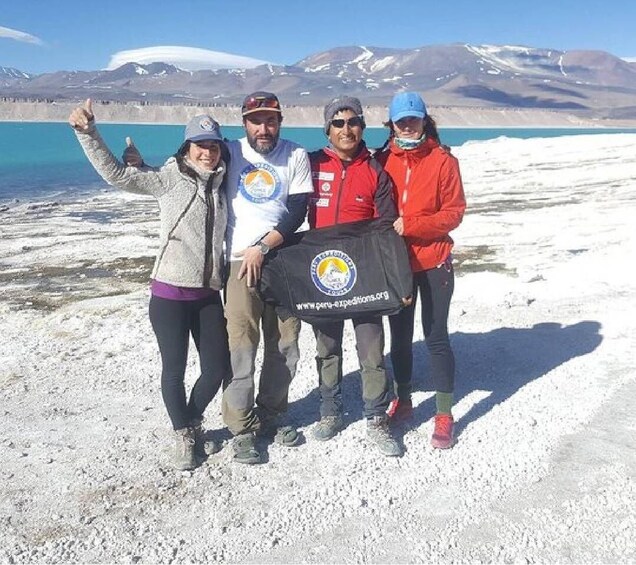 A group of people standing on a rocky terrain with a lake and mountains in the background. 4