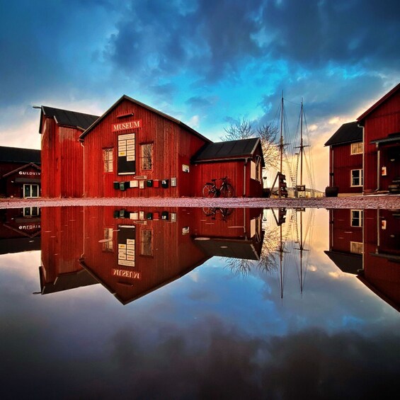 A red wooden building labeled 'Museum' with a bicycle parked outside, reflecting in a calm body of water. 4