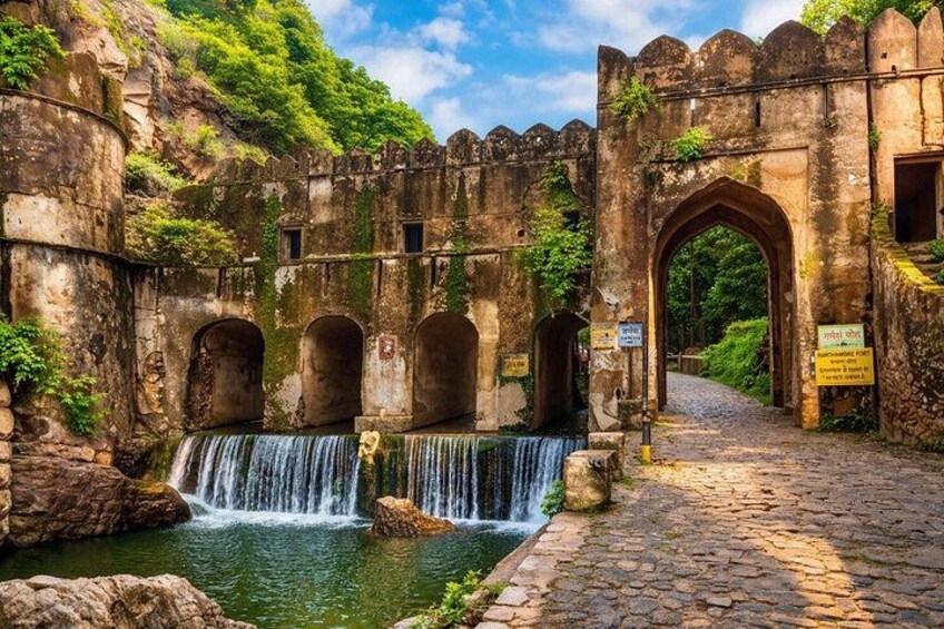 A historic stone bridge with a waterfall, lush greenery, and an arched entrance. 3