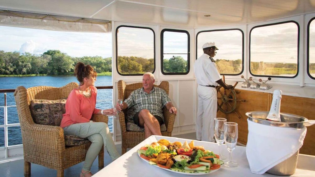 A boat with wicker furniture, a table with a salad, and a person in a white uniform. 1
