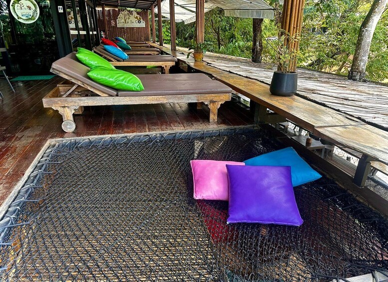 A covered outdoor lounge area with wooden benches and lounge chairs, a woven floor mat, and potted plants. 4