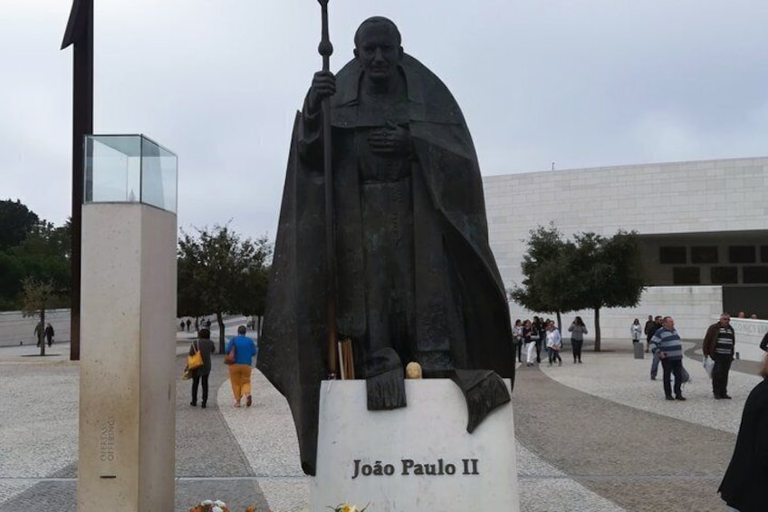 Eine Statue von Johannes Paul II. auf einem öffentlichen Platz, an dem Menschen herumlaufen. 3