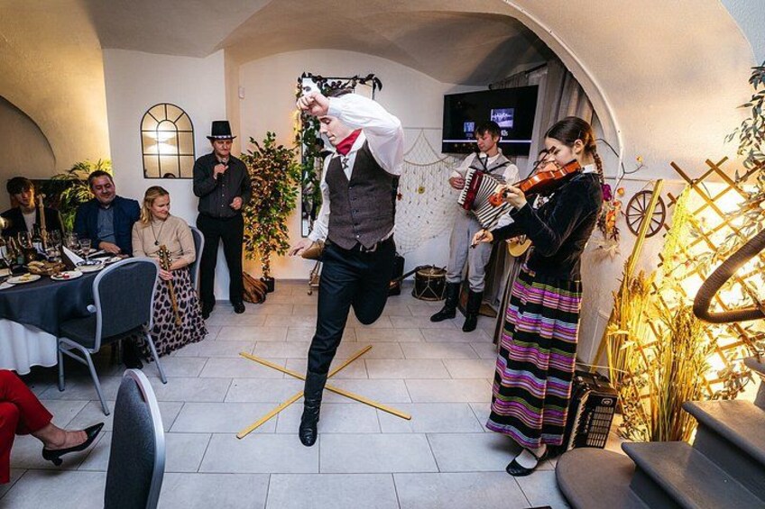 En mand spiller violin, en kvinde spiller fløjte, og en mand spiller tromme i et rum med borde og stole. 1