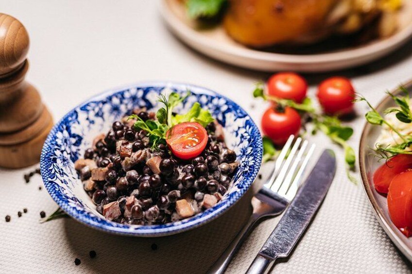 Un tazón de frijoles negros con una rodaja de tomate encima, un tenedor, un cuchillo y un molinillo de pimienta sobre una mesa. 2