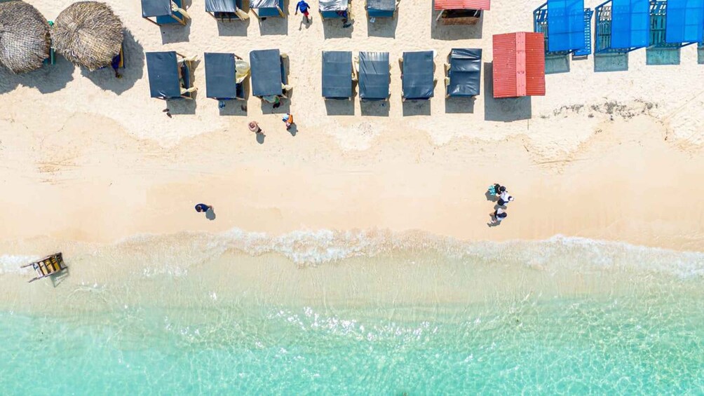A beach with sun loungers, a few people walking, and a small boat near the water. 1