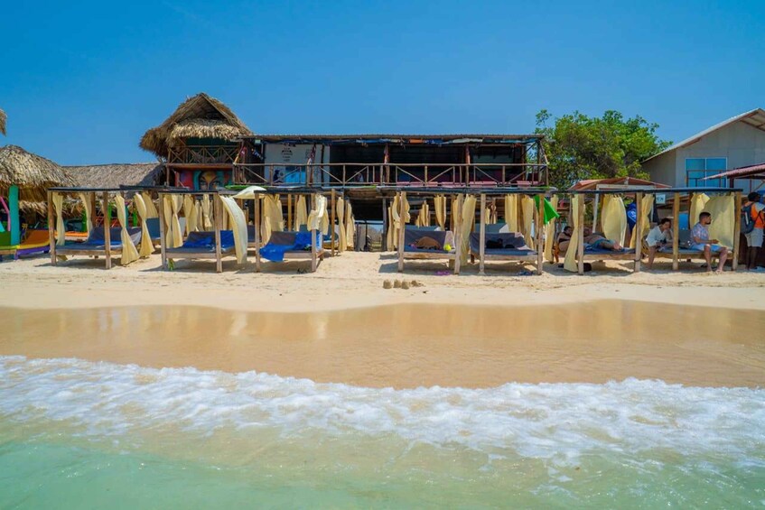 A beach with thatched-roof huts and a building with a balcony. 2