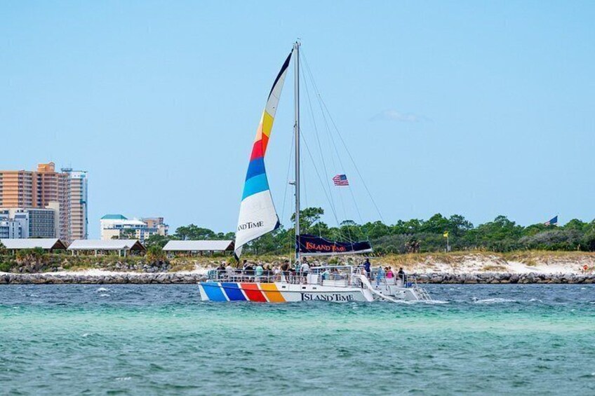 Una barca a vela con una vela colorata, chiamata 'Island Breeze', che naviga su acque limpide con una città sullo sfondo. 2