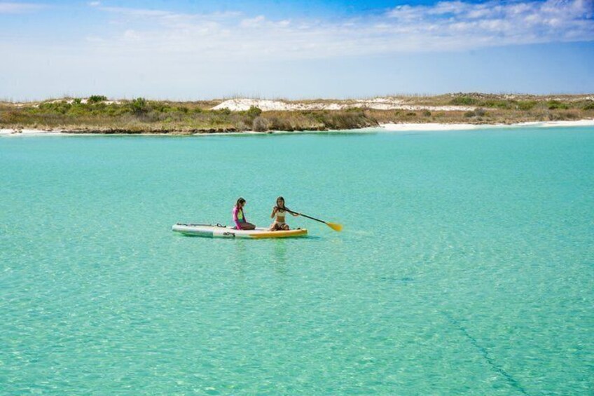 Two people in a small boat on clear turquoise water with a beach and vegetation in the background. 5