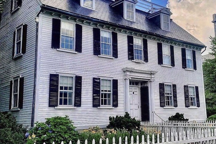 A two-story house with a white exterior and black shutters, surrounded by a white picket fence. 2