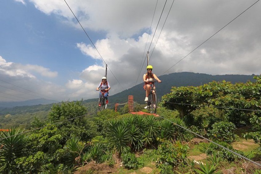 Two people on a zipline, surrounded by lush greenery and mountains in the background. 1