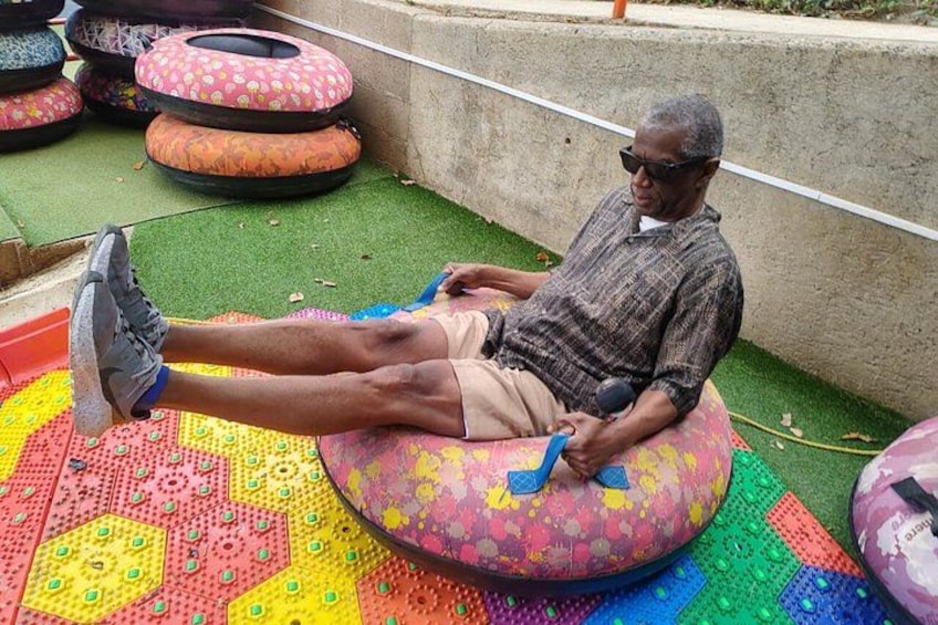 A man sitting on a colorful inflatable tube on a patterned mat, surrounded by similar tubes. 4