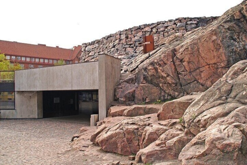 A modern building with a concrete facade, a stone wall, and large rocks in the foreground. 3