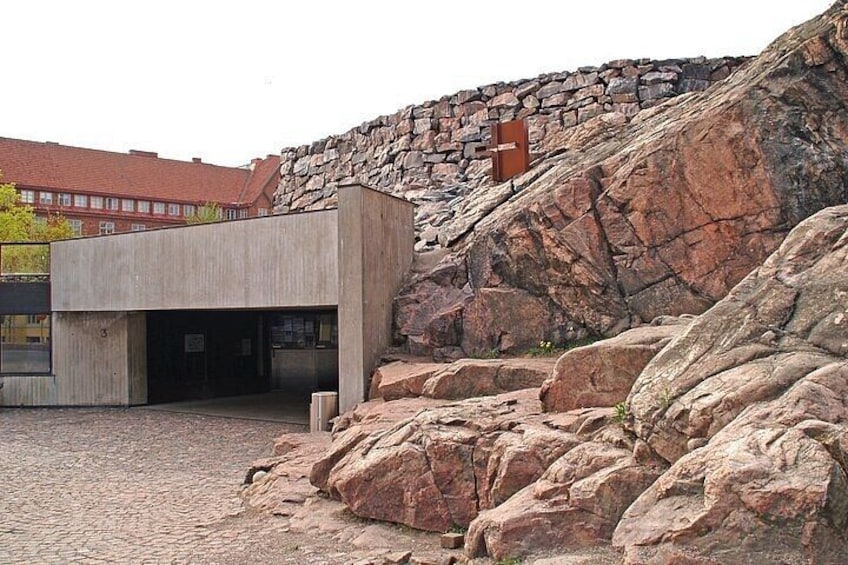 A modern building with a concrete facade, a stone wall, and large rocks in the foreground. 3