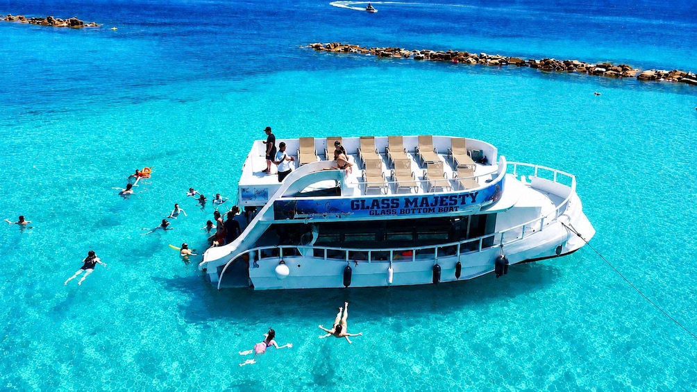 A glass-bottom boat named 'Glass Majesty' with people swimming and lounging around it. 2