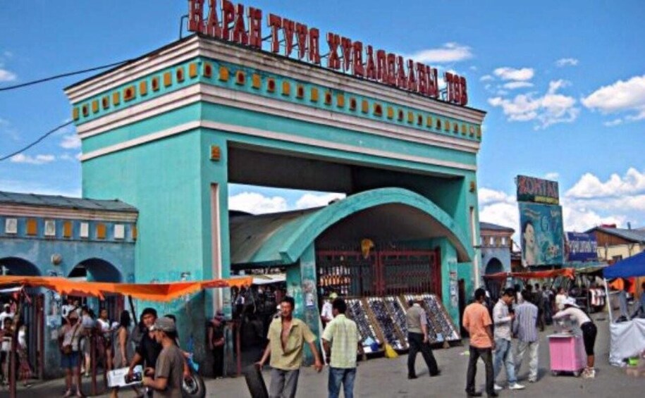 A turquoise archway with a sign above it, surrounded by market stalls and people. 3