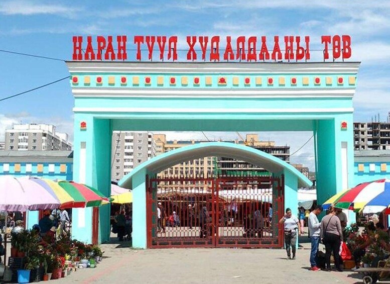 A turquoise archway with red text, surrounded by market stalls and people. 1