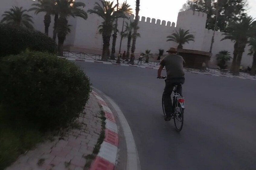 Une personne à vélo sur une route asphaltée, avec des palmiers et un grand bâtiment en arrière-plan. 3