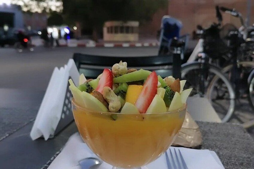 Une salade de fruits servie dans un saladier en verre, posée sur une table avec une serviette et une fourchette. 4