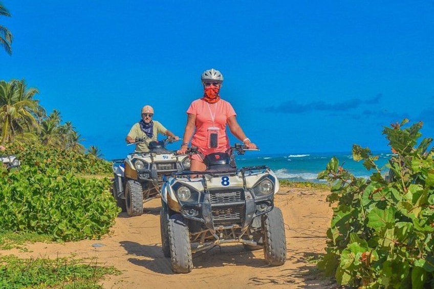 Twee personen rijden op quadbikes over een zandpad, met een strand en de oceaan op de achtergrond. 4