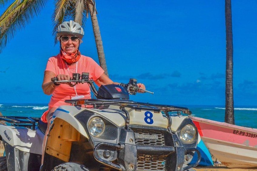 Iemand rijdt op een quad over een strand, met palmbomen en de oceaan op de achtergrond. 3