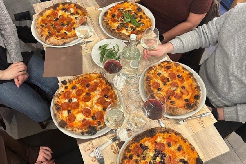 A group of people seated around a table with large pizzas and glasses of wine. 2