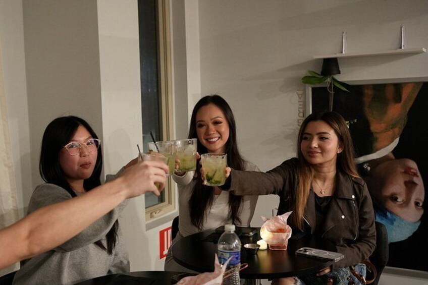 Tres personas brindando con bebidas en una mesa con una botella y una copa. 2