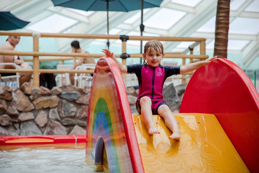 A child sliding down a colorful water slide in a covered area with stone walls and umbrellas. 4