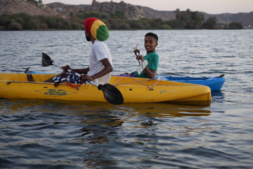 Two people in a yellow kayak on a calm body of water with a hilly landscape in the background. 2